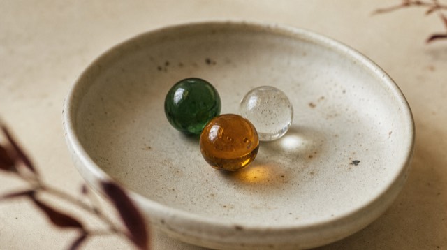 Abstract still life: three different coloured glass beads of amber, ink green and clear resting together in a shallow ceramic bowl