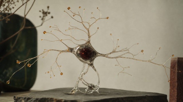 Abstract still life: a delicate branching glass sculpture resembling a neuron, with fine filaments ending in tiny amber droplets