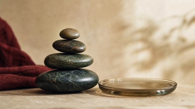 Abstract still life: a set of smooth river stones balanced in a descending cascade, each slightly smaller, beside a shallow glass dish of still water
