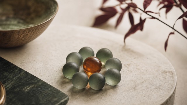 Abstract still life: a cluster of small frosted glass spheres forming a protective ring around one amber sphere