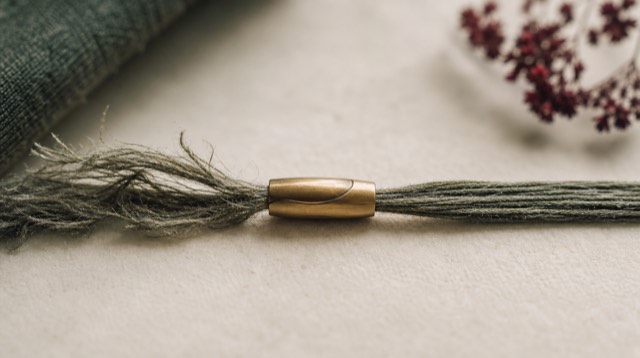 Abstract still life: a strand of woven linen thread being rejoined by a single brass needle-free clasp, frayed fibres turning into neat parallel strands