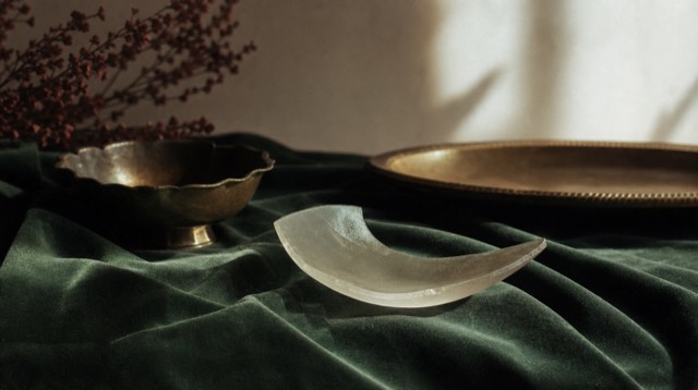 Abstract still life: a pale crescent of frosted glass resting on deep green velvet, with soft blue-hour light and long shadows