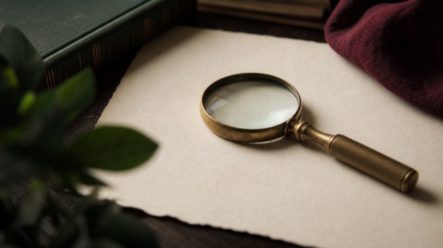 Abstract still life: a magnifying glass resting on a pale map-like paper texture with no text