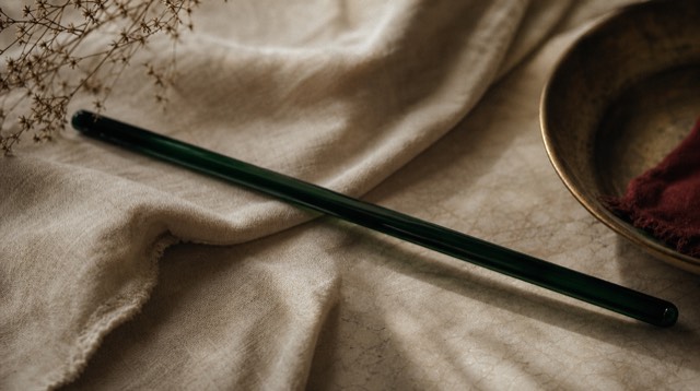 Abstract still life: a single long ink-green glass rod lying diagonally across folded linen