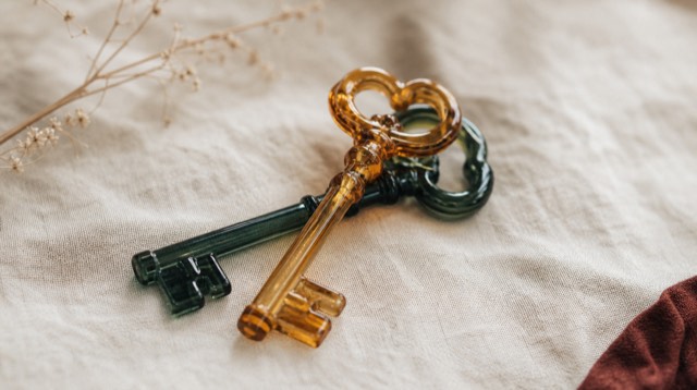 Abstract still life: two glass keys, amber and ink green, crossed on a linen cloth